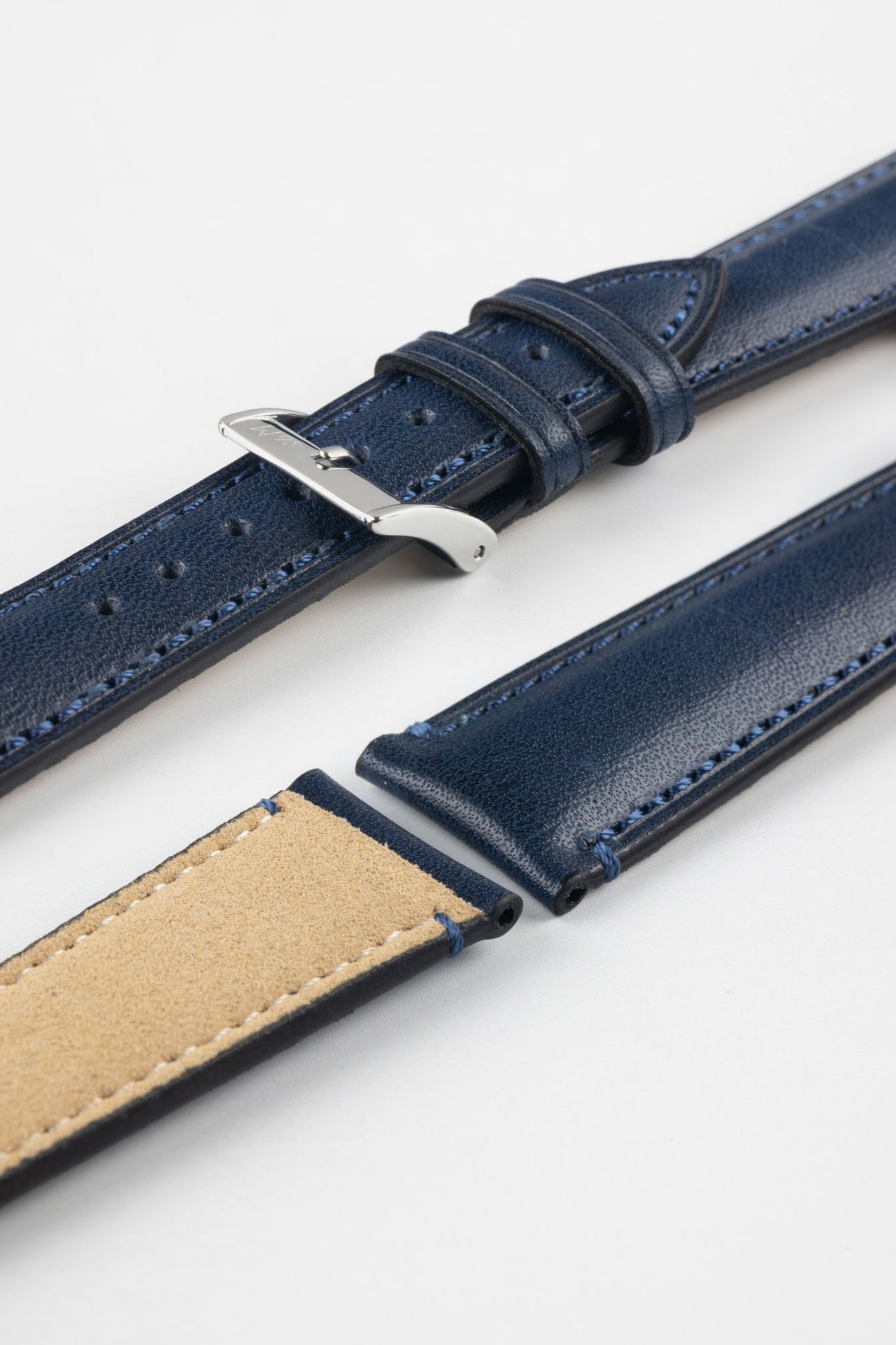 Blue leather watch strap with matching stitching, shown in angled close-up with a silver buckle, adjustment holes, and beige suede underside.