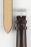 Close-up of a brown leather watch strap showing a silver buckle, adjustment holes, and beige suede underside on a light grey background.