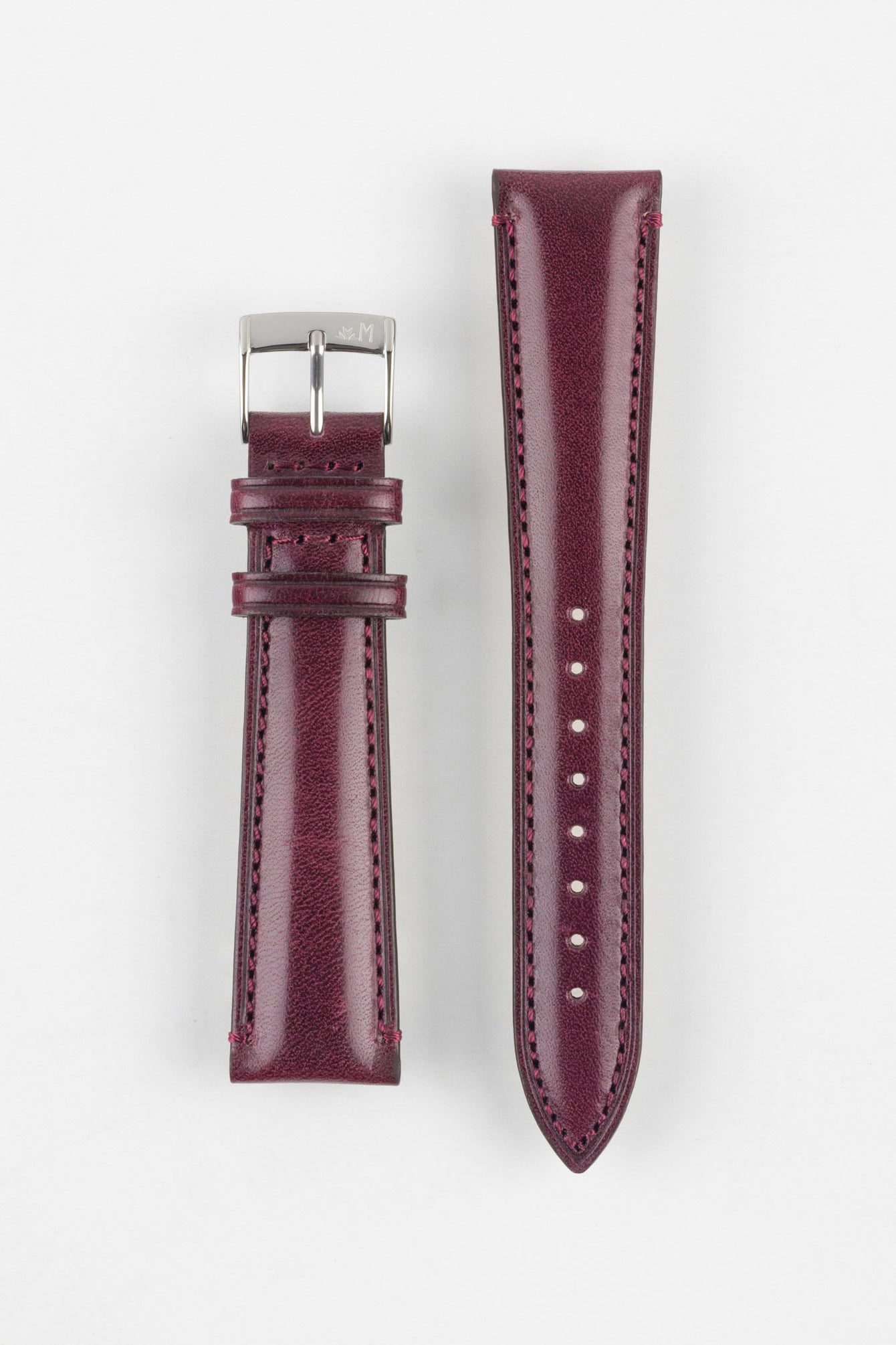Product shot of a two-piece burgundy leather watch strap laid flat on a plain light background. The strap features a smooth, slightly textured finish with matching burgundy stitching and a gently padded profile. One piece is fitted with a polished silver pin buckle engraved with a small logo, while the other tapered piece displays multiple adjustment holes, highlighting the craftsmanship, stitching detail, and rich leather tone.
