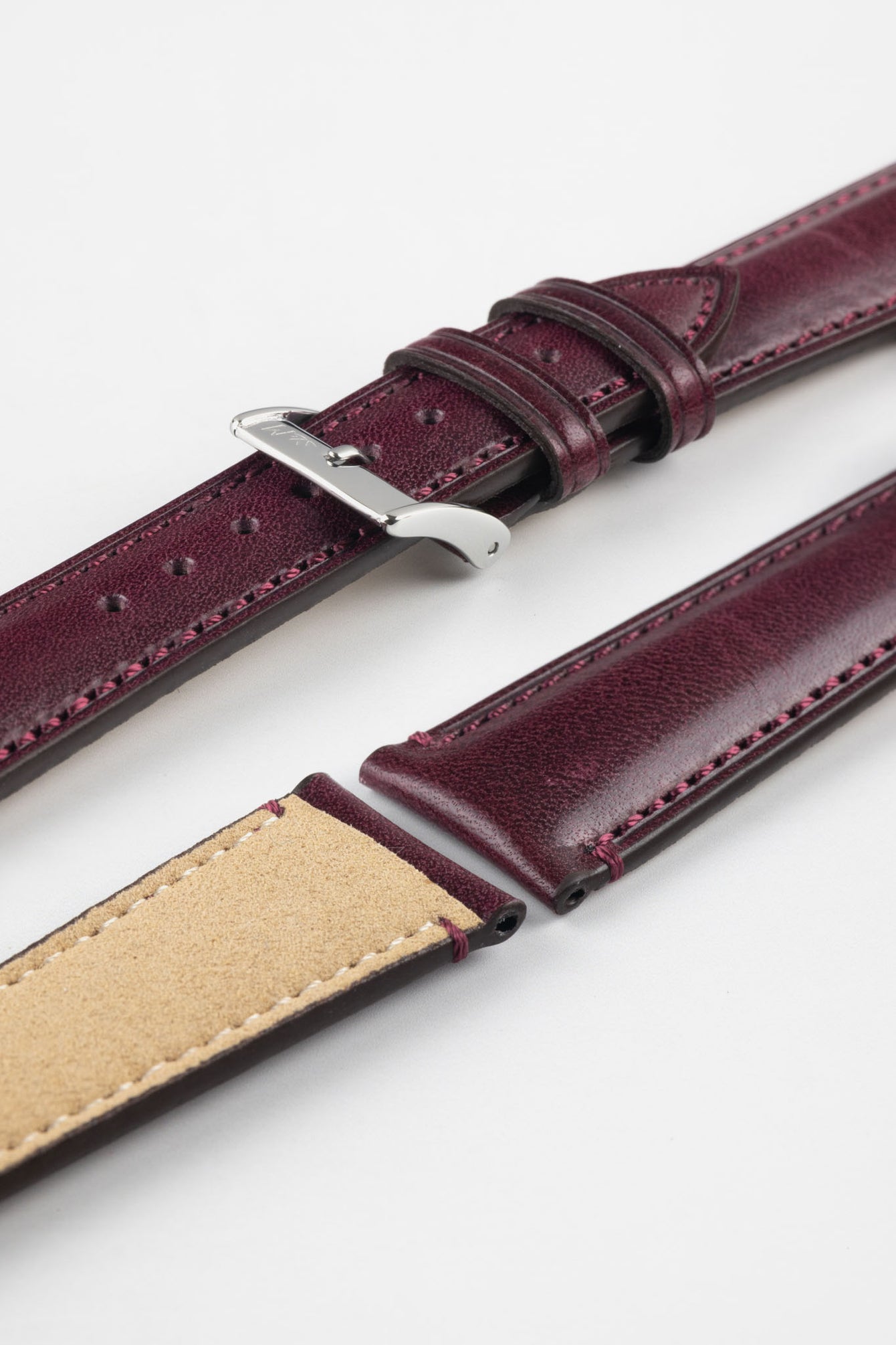 Burgundy leather watch strap with matching stitching, shown in angled close-up with a silver buckle, adjustment holes, and beige suede underside.
