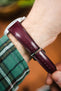 Close-up of a burgundy leather watch strap with a glossy finish and matching stitching, secured on a wrist with a polished silver buckle and multiple adjustment holes.