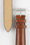 Close-up of a tan-brown leather watch strap showing a silver buckle, adjustment holes, and beige suede underside on a light grey background.