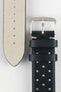 
A close-up, high-angle shot of a black Morellato Brahms watch strap laid against a white background. The image focuses on the steel buckle and the underside of the longer strap piece, revealing its light-coloured, soft suede-like lining.