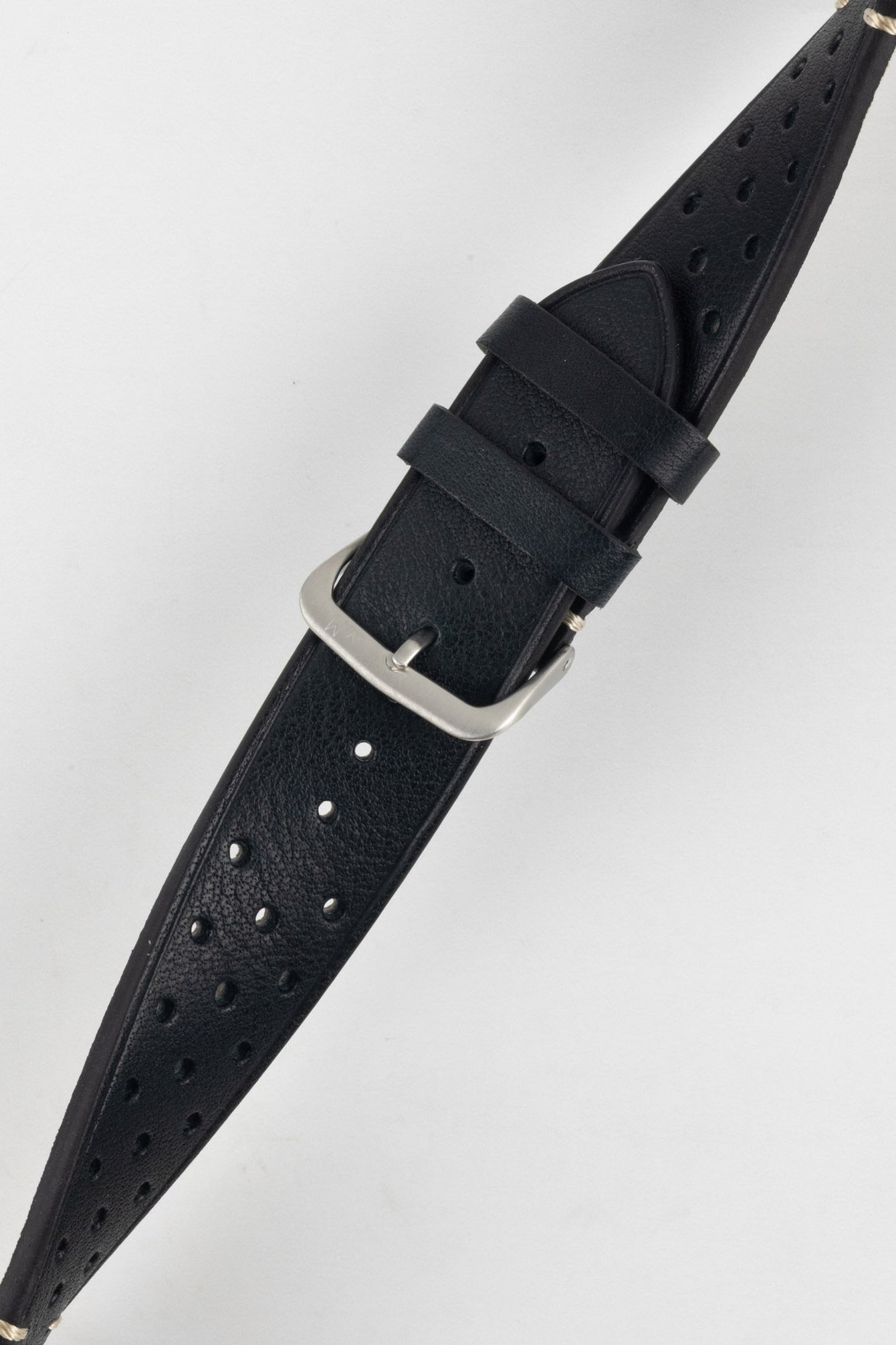
A close-up, high-angle shot of a black Morellato Brahms watch strap, buckled and resting diagonally against a white background. The image focuses on the rally-style perforations and the satin-finished steel buckle.