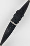 
A close-up, high-angle shot of a black Morellato Brahms watch strap, buckled and resting diagonally against a white background. The image focuses on the rally-style perforations and the satin-finished steel buckle.