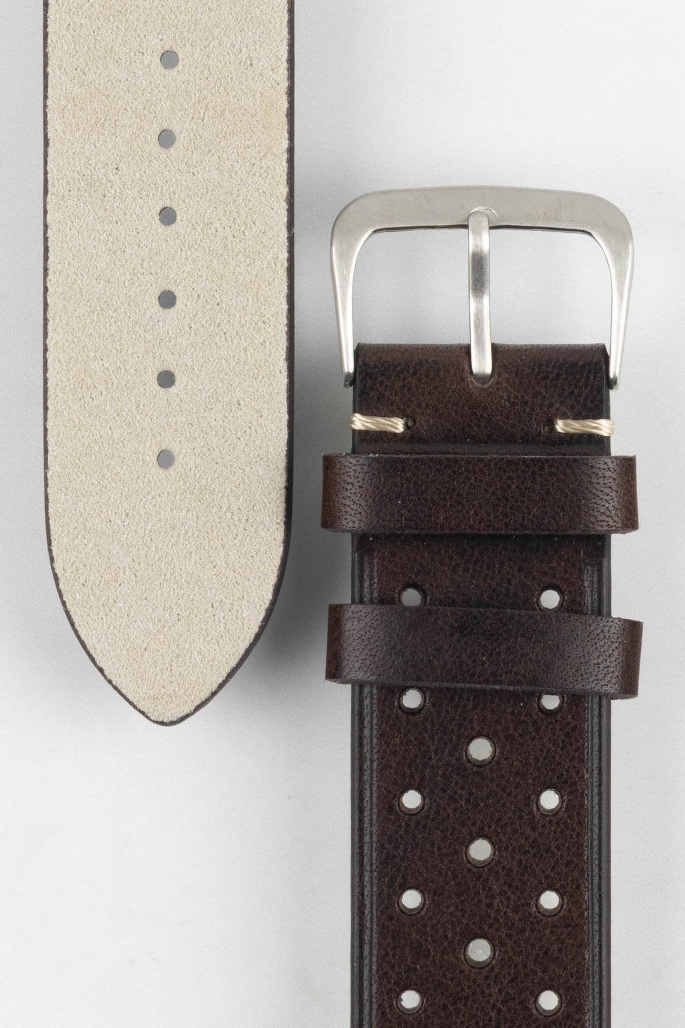 A close-up, high-angle shot of a dark brown Morellato Brahms watch strap laid against a white background. The image focuses on the steel buckle and the underside of the longer strap piece, revealing its light-coloured, soft suede-like lining.