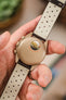 A close-up of the back of a hand holding an Omega x Swatch MoonSwatch 'Jupiter' watch, showing the light brown case back with the 'MISSION TO JUPITER' text and an image of the planet Jupiter. The watch is on a dark brown Morellato Brahms perforated leather strap, with the perforated cream-coloured lining clearly visible.