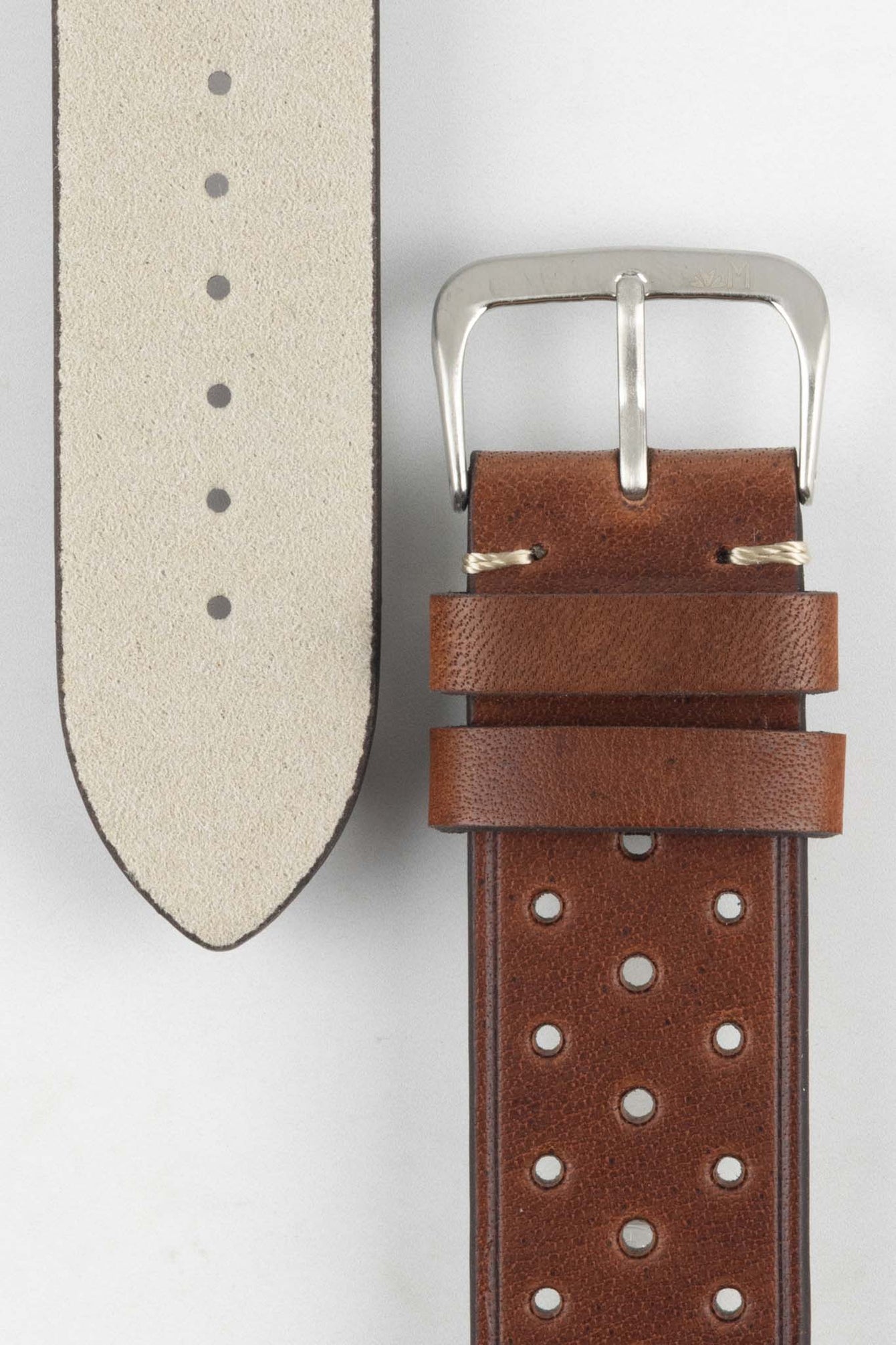 
A close-up, high-angle shot of a medium brown, 'gold' Morellato Brahms watch strap laid against a white background. The image focuses on the steel buckle and the underside of the longer strap piece, revealing its light-coloured, soft suede-like lining.