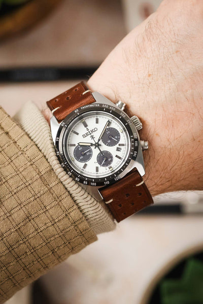 A high-angle shot of a man's wrist wearing a Seiko Speedtimer chronograph watch on a medium brown Morellato Brahms perforated leather strap. The watch has a white dial with three black sub-dials and a black bezel. The man is wearing a tan sweater.