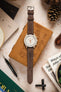 Overhead shot of a Morellato SCHUMANN brown suede watch strap with an Omega MoonSwatch and other accessories.