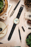 Black Tiepolo crocodile grain strap with a Studio Underdøg watch laid out on a table with other watch accessories.