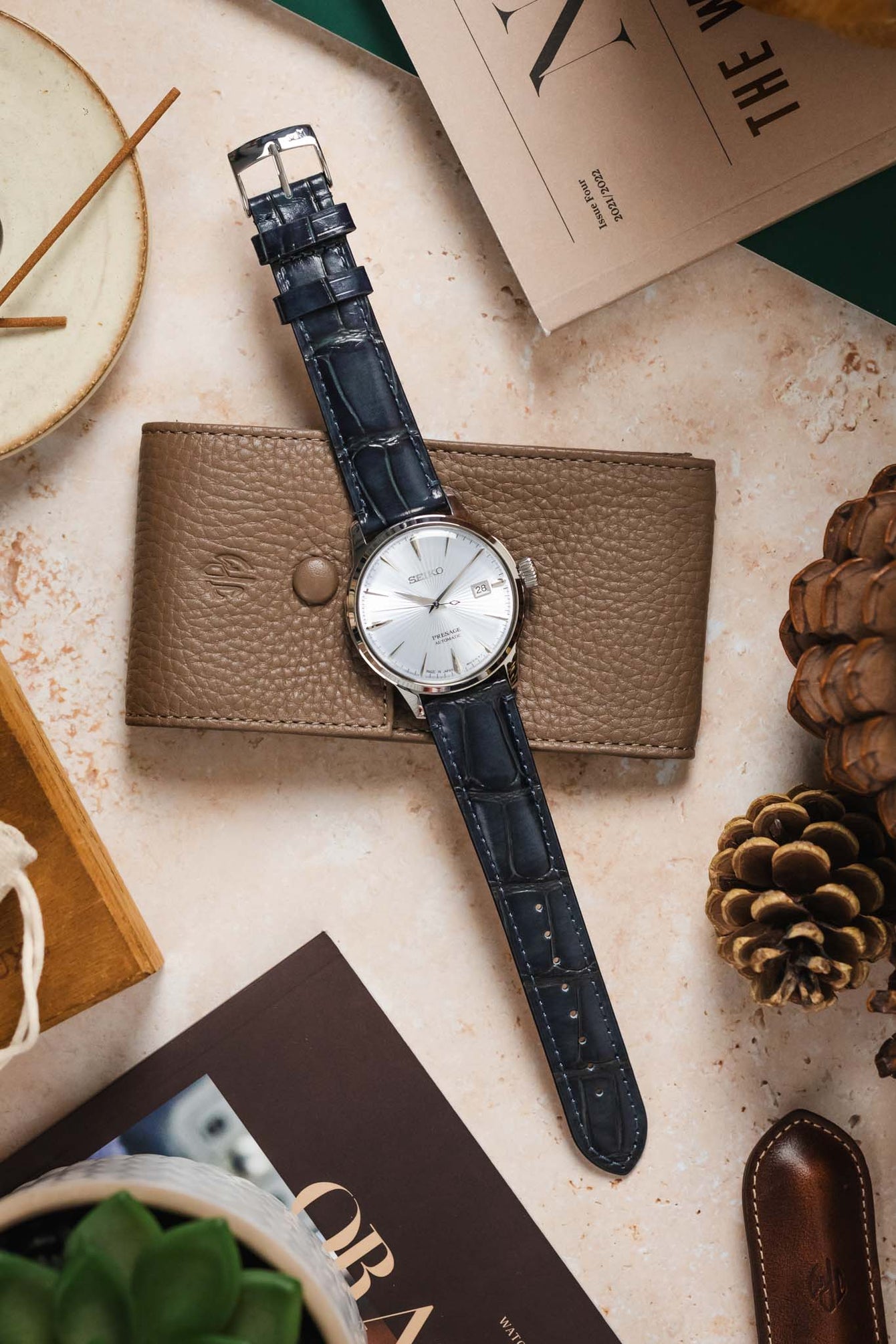 A Seiko Presage watch with the blue Morellato Tiepolo strap laid out with a brown wallet and other accessories.