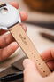 A person's hands holding an Omega watch, showing the back of the burgundy Morellato Tiepolo watch strap.