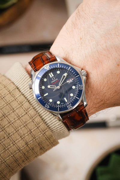 A man's wrist wearing an Omega Seamaster watch with a light brown Morellato Tiepolo leather strap.