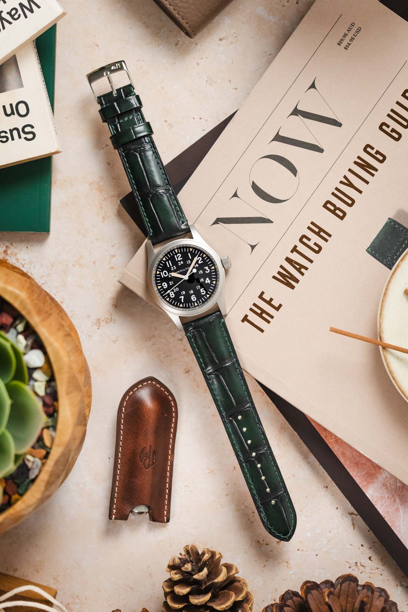 A Hamilton Khaki Field watch with the Morellato Tiepolo green strap laid out with other watch enthusiast accessories.