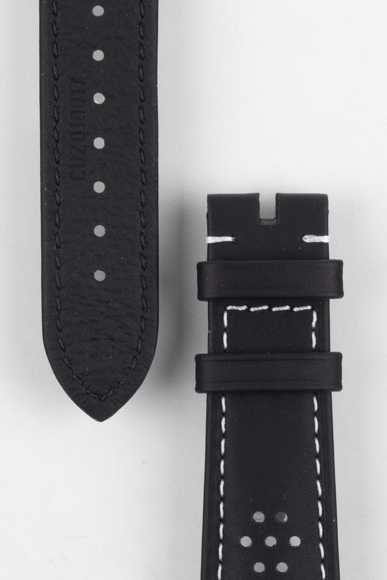 Close-up product image of a black leather watch strap against a white background, showing the underside with multiple adjustment holes and faint embossed text on one piece, and the other section with two keepers, white contrast stitching, and perforated detailing near the lug end.