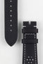Close-up product image of a black leather watch strap against a white background, showing the underside with multiple adjustment holes and faint embossed text on one piece, and the other section with two keepers, white contrast stitching, and perforated detailing near the lug end.