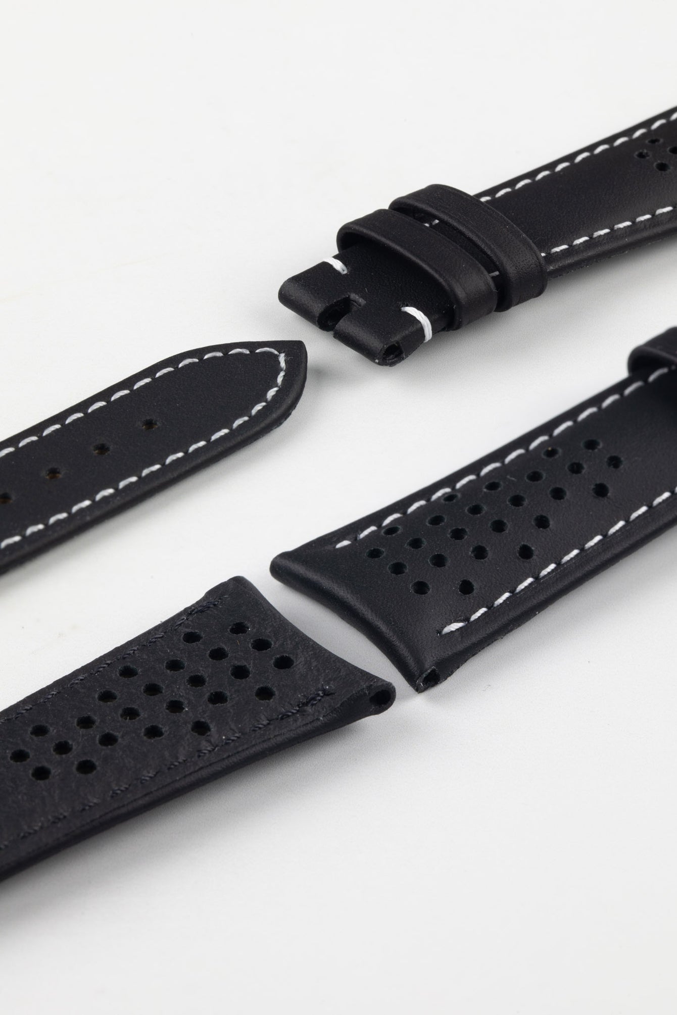 Close-up product image of a black perforated leather watch strap against a white background, showing multiple sections with ventilation holes, white contrast stitching, and the end with two keepers, highlighting the smooth, slightly padded texture and sport-style design.
