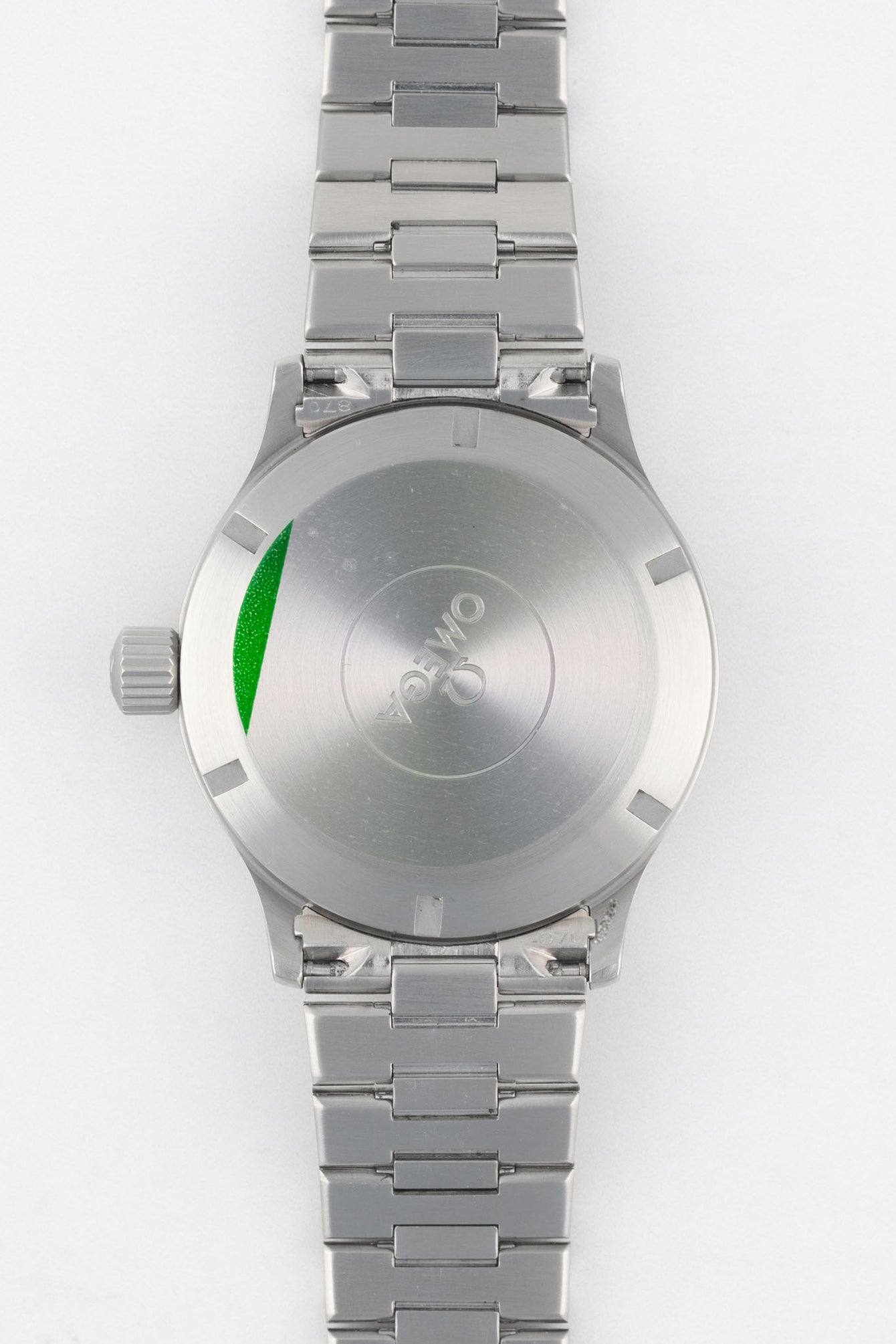 A direct view of the stainless steel case back, featuring the Omega logo in the center and a partial green protective sticker on the left edge.