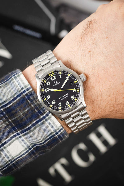 A close-up of the watch being worn on a wrist, paired with a blue and white plaid flannel shirt, showing how the 36mm case sits on the arm.