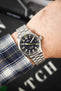 A close-up of the watch being worn on a wrist, paired with a blue and white plaid flannel shirt, showing how the 36mm case sits on the arm.