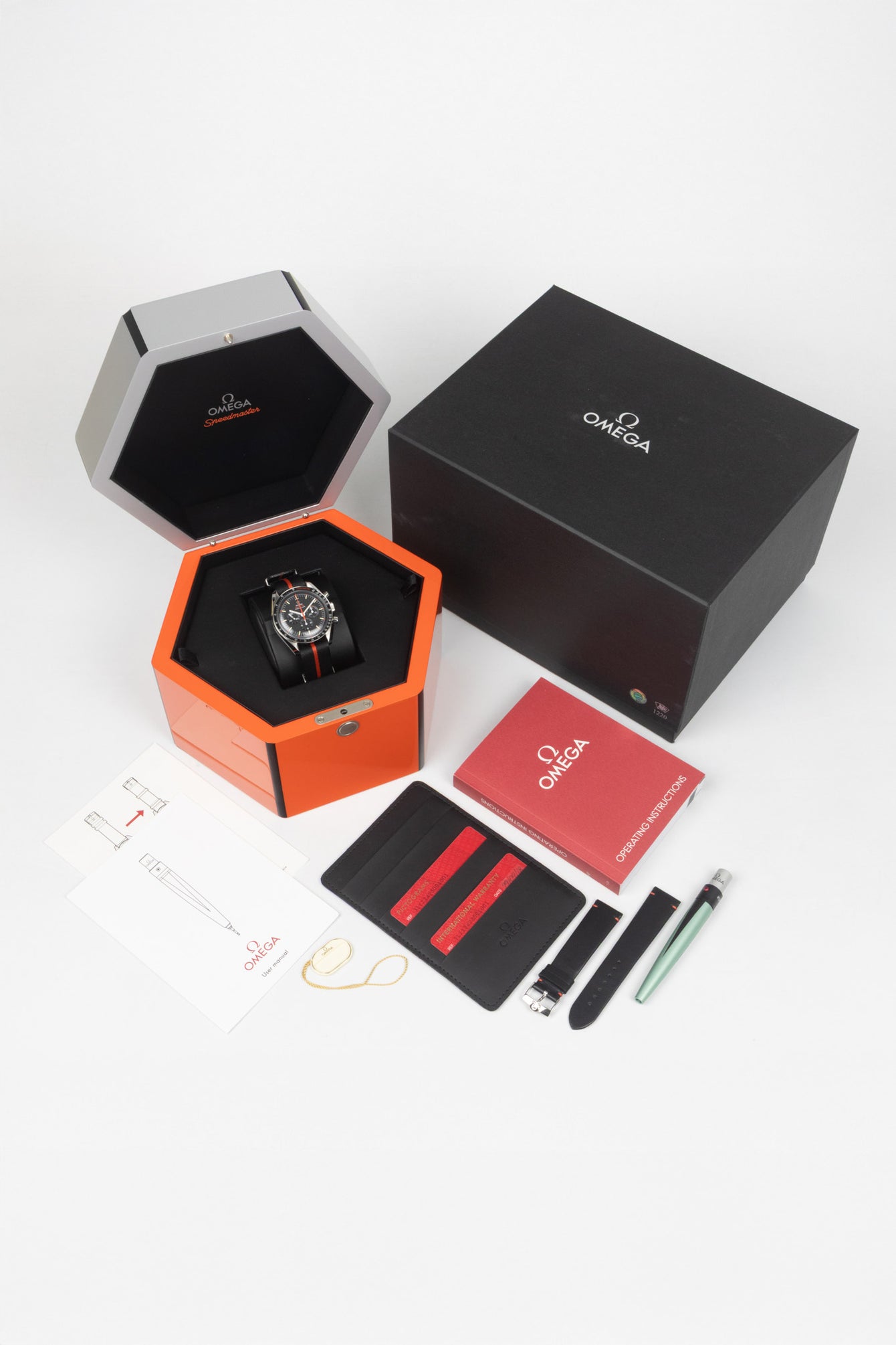 A box and contents photography of an Omega Ultraman Speedy Tuesday showing full box and papers including the black light and spare leather watch strap.