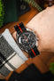 An overhead wrist shot of an Omega Speedy Ultraman, its being worn on a black and orange nylon strap with a grey jumper sleeve and checked jacket.