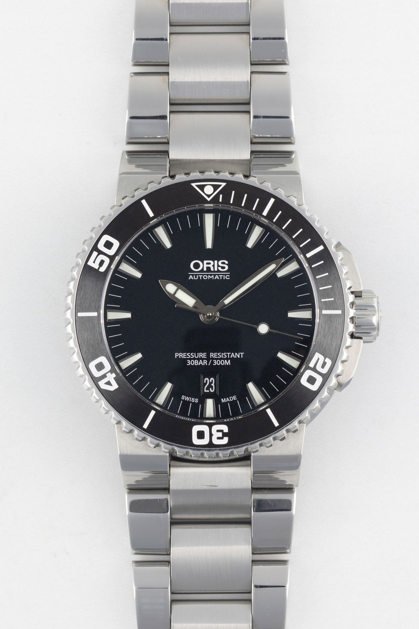 A direct, front-facing studio photograph of an Oris Aquis Date watch with a black dial, white date window at 6 o'clock, and an integrated stainless steel bracelet on a white background.