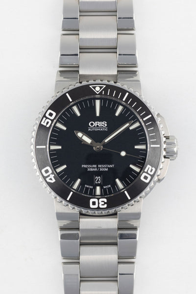 A direct, front-facing studio photograph of an Oris Aquis Date watch with a black dial, white date window at 6 o'clock, and an integrated stainless steel bracelet on a white background.