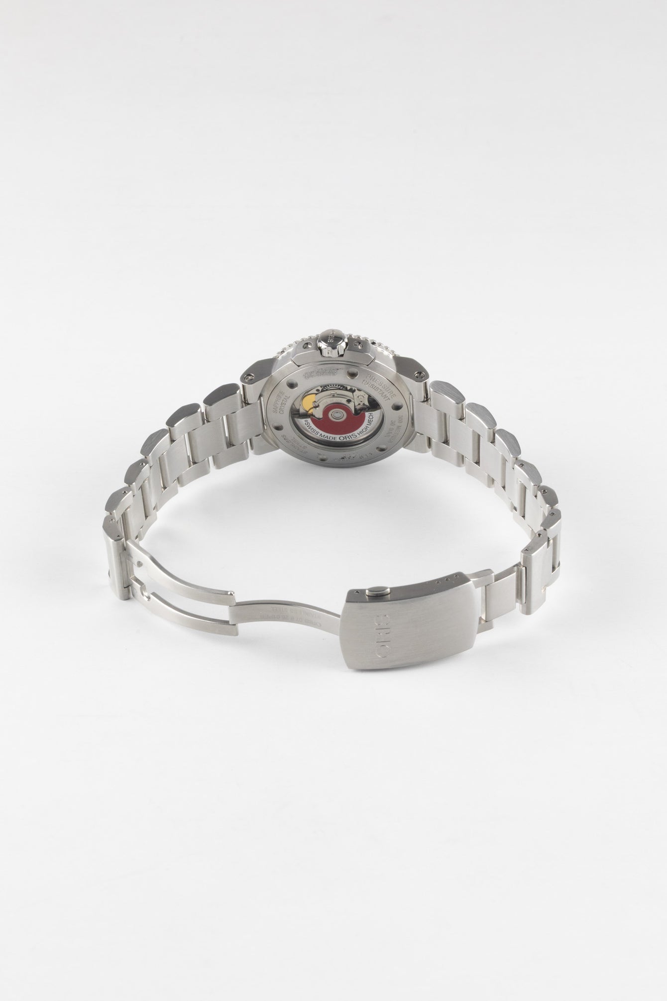 An angled view of the open stainless steel bracelet and case back of an Oris Aquis Date, showcasing the exhibition window and the signature red Oris automatic rotor.