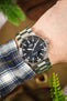A wrist shot of a person wearing an Oris Aquis Date with a stainless steel bracelet, paired with a blue, grey, and white checkered flannel shirt.