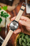A hand holding a Seiko watch, showing the underside of the watch and the black RIOS1931 Montana strap with its brand, model, and size markings stamped on the leather lining.