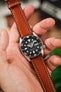 A hand holding a Seiko diving watch on a cognac-colored RIOS1931 Montana leather watch strap with white contrast stitching.
