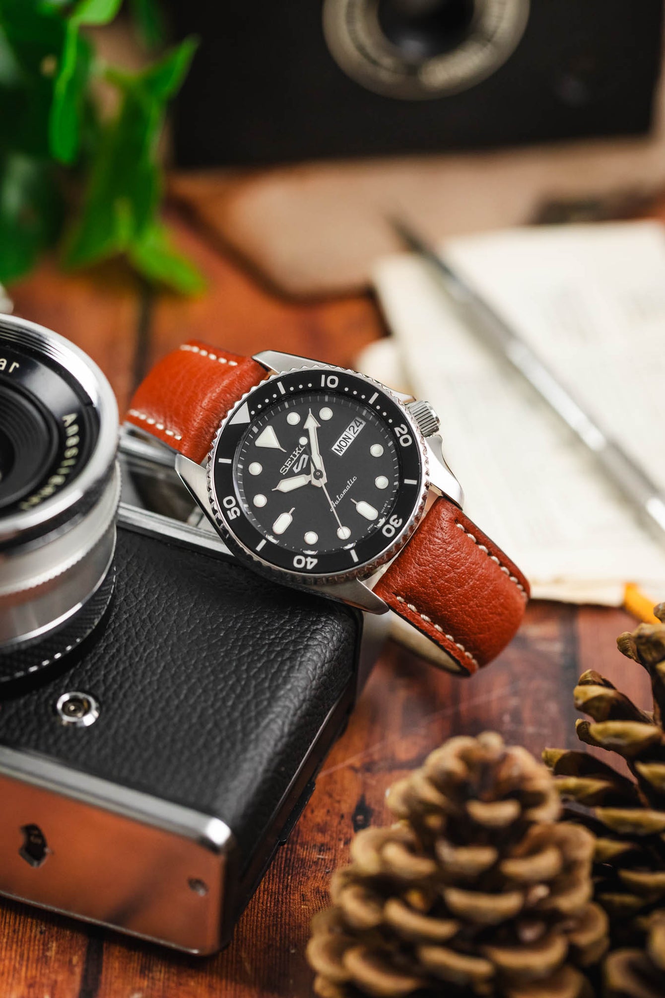 A Seiko diving watch on a cognac-colored leather RIOS1931 Montana strap, photographed on a wooden surface with a vintage camera.