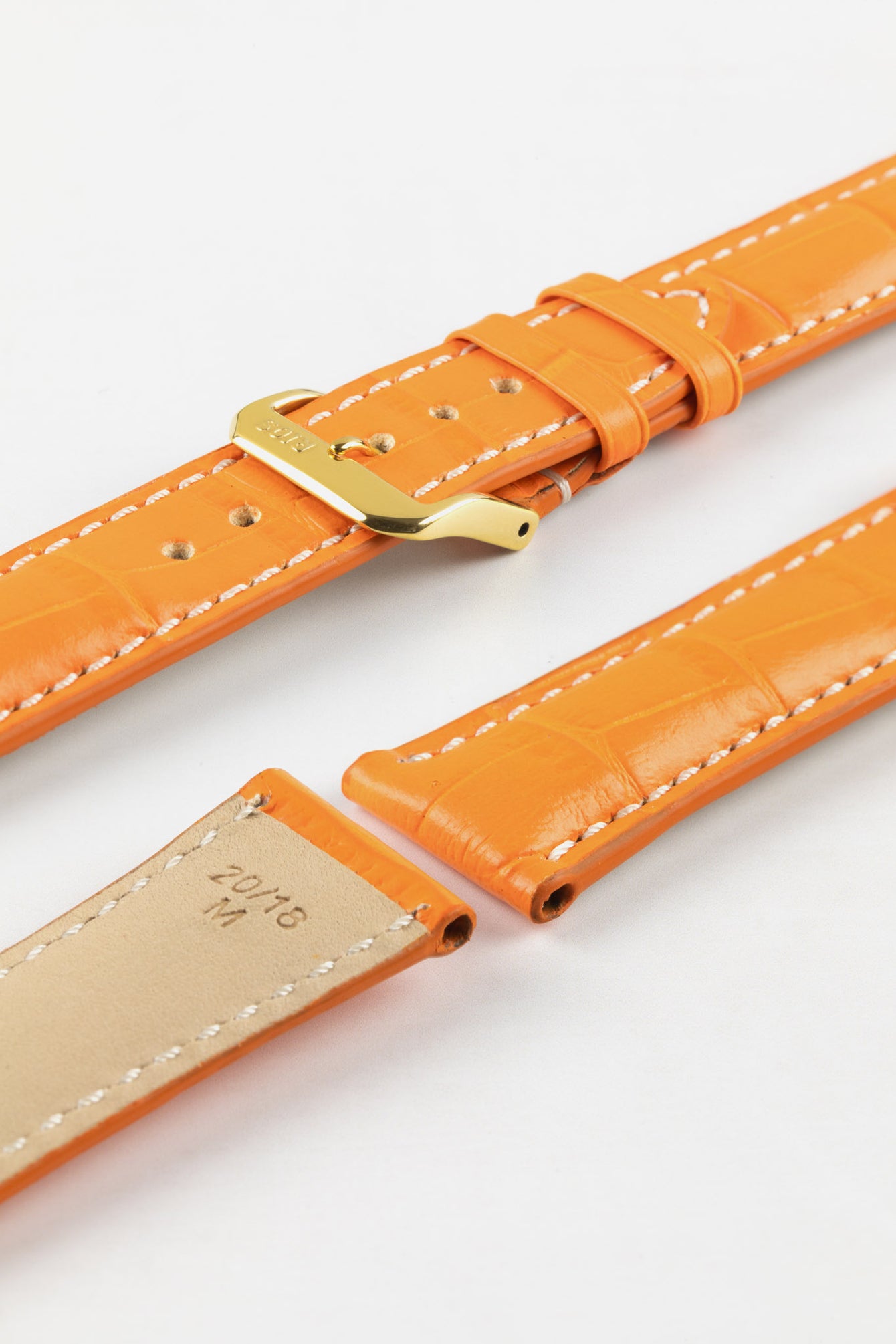 A product shot of an orange crocodile-embossed leather watch strap with a gold-plated buckle and white contrast stitching. The two separate pieces of the strap are laid diagonally on a plain white background, revealing the tan underside of one piece with the size "20/18" stamped on it.