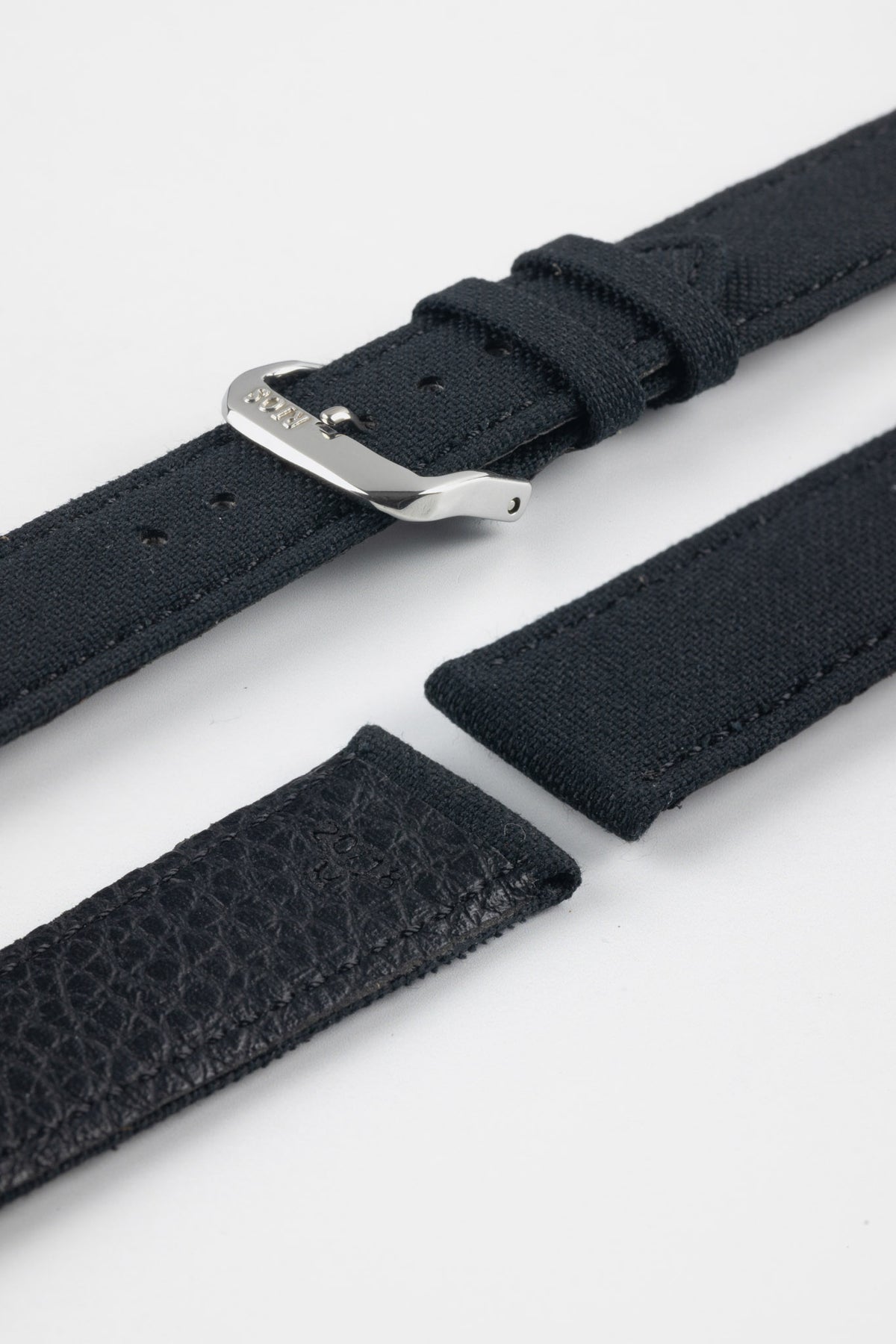 Close-up product image of a dark navy watch strap with a polished silver buckle. The strap is shown in separated sections, highlighting the fabric exterior, stitching details, adjustment holes, and textured leather underside against a light gray background.