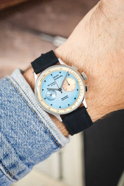 Studio Underd0g Bicompax chronograph watch on a black canvas strap, shown on wrist with a light blue dial and stainless steel case.