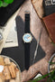 Studio Underd0g Bicompax chronograph watch on a black canvas strap, displayed with vintage accessories on a rustic wooden surface.
