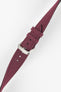 Close-up angled view of a burgundy fabric watch strap on a light gray background. The strap features a woven textile texture, stitched edges, multiple adjustment holes, and a polished silver-tone RIOS-branded buckle with two matching fabric keepers. The image highlights the strap’s tapered shape, rich burgundy color, and refined construction details.