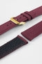 Close-up product image of a burgundy fabric watch strap displayed in separate sections on a light gray background. The strap features a polished gold-tone RIOS-branded buckle, matching fabric keepers, and stitched edges. A section of the black textured leather underside with burgundy contrast stitching is visible, highlighting the combination of woven fabric and leather backing, along with the strap’s premium construction and detailing.