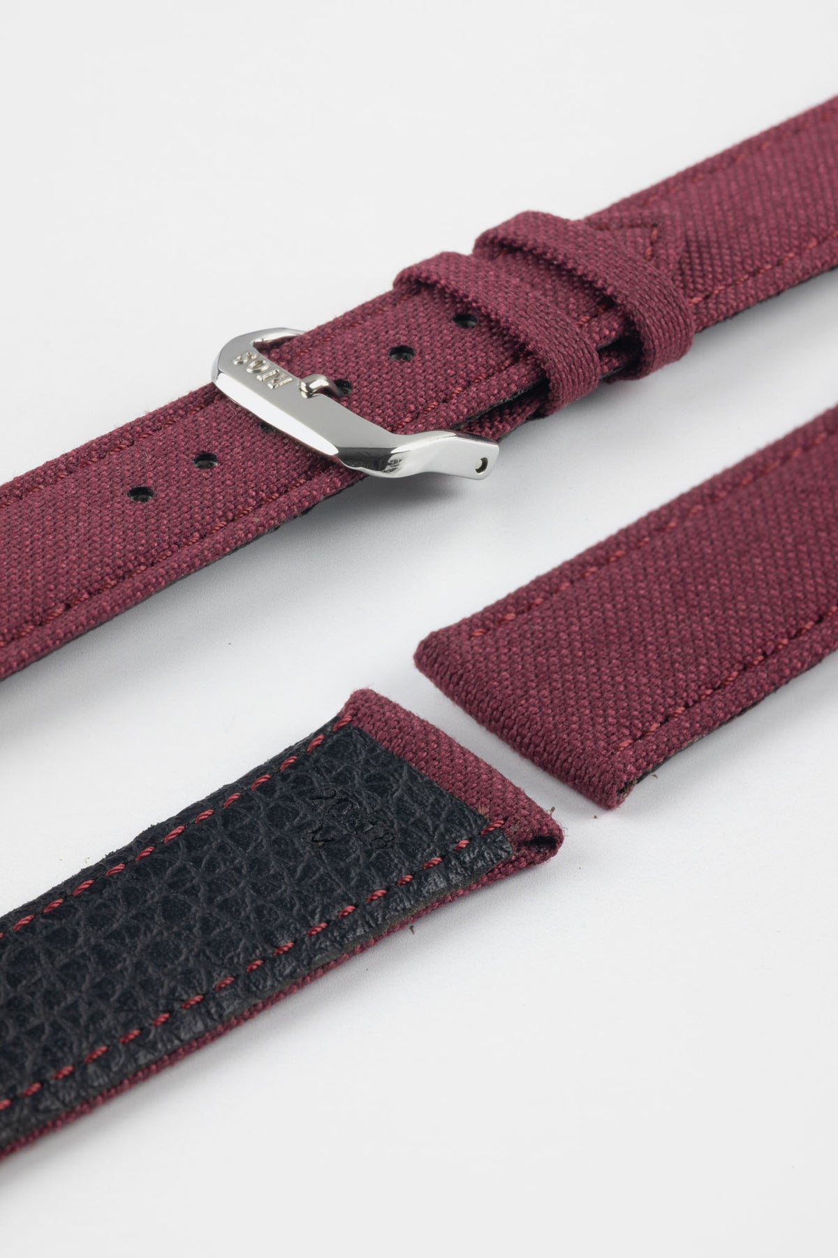 Close-up product image of a burgundy fabric watch strap displayed in separate sections on a light gray background. The strap features a polished silver-tone RIOS-branded buckle, matching fabric keepers, and stitched edges. A section of the black textured leather underside with burgundy contrast stitching is visible, highlighting the combination of woven fabric and leather backing, along with the strap’s premium construction and detailing.