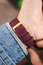 Burgundy canvas watch strap with a gold-tone RIOS1931 buckle, shown on wrist from the underside.