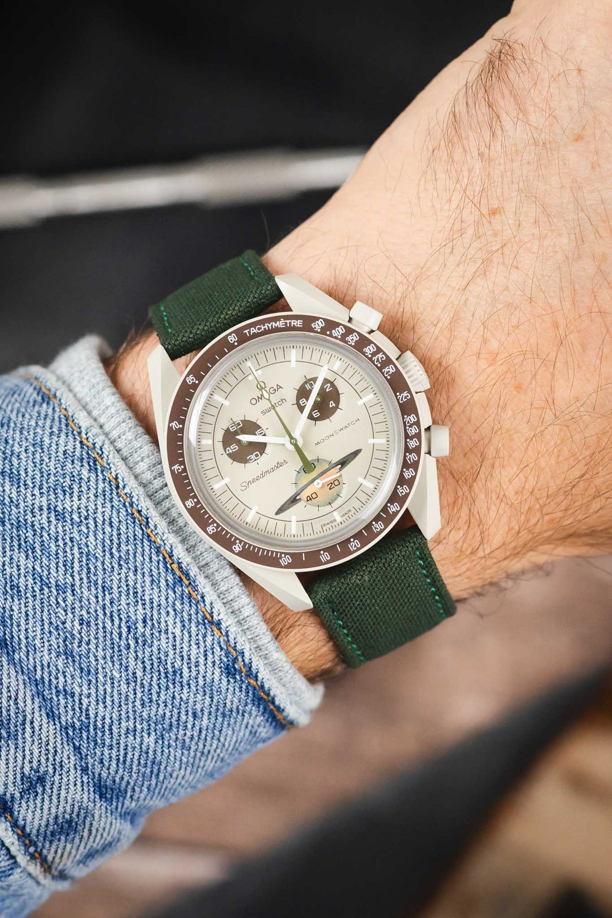 Omega x Swatch MoonSwatch Mission to Jupiter on an olive green canvas strap, shown on wrist with a cream dial and beige case.