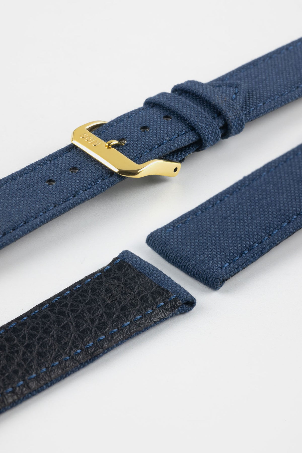 Close-up product image of an ocean blue fabric watch strap displayed in separate sections on a light gray background. The strap features a polished gold-tone RIOS buckle, matching fabric keepers, and stitched edges. A portion of the textured black leather underside is visible, highlighting the contrast between the woven fabric exterior and leather backing, along with the strap's construction and finishing details.