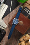 Tudor Black Bay dive watch on an ocean blue canvas strap, displayed with vintage accessories on a rustic wooden surface.