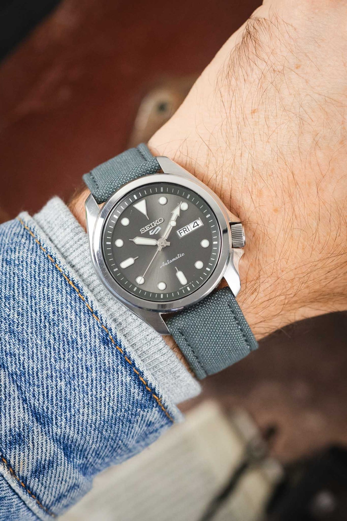 Seiko 5 automatic watch on a stone grey canvas strap, shown on wrist with a grey dial and stainless steel case.