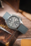 Seiko 5 automatic watch on a stone grey canvas strap, displayed on a vintage book with a watchmaker’s screwdriver.