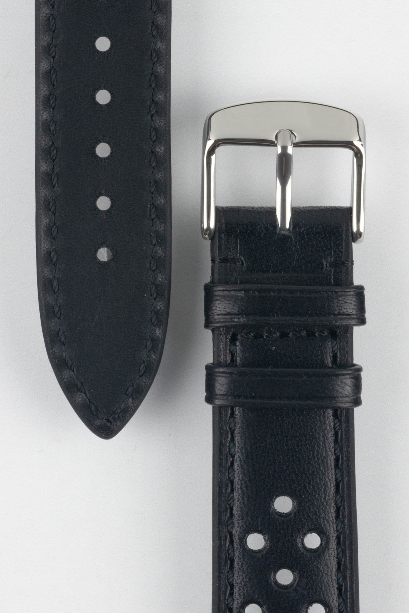 Close-up product shot of a black perforated leather watch strap paired with a separate strap piece, both featuring matching black stitching. A polished silver pin buckle is attached to the main strap, and the components are positioned on a plain light background to highlight the smooth leather texture, perforations, stitching details, and buckle hardware.