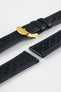Close-up product shot of black perforated leather watch strap components with matching black stitching, including one fitted with a polished gold-tone deployment clasp. Additional strap sections are arranged on a plain light background, highlighting the leather grain, perforations, stitching detail, and gold clasp hardware.