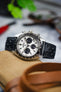 Close-up of a Seiko Speedtimer chronograph watch featuring a white panda dial with three dark blue sub-dials, black tachymeter bezel, and brushed stainless steel case, fitted with a black perforated leather rally strap. Displayed on a canvas pouch alongside leather accessories, sunglasses, and watch tools, the image highlights the strap's smooth leather finish, motorsport-inspired perforations, and premium handcrafted construction.